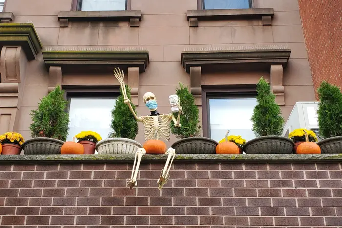 A Halloween skeleton wears a surgical masks and holds a cup of coffee on a Brooklyn rooftop.